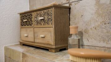 Un mueble de madera con diseños tallados elaborados, una botella pequeña y un cepillo de madera sobre una superficie de baldosas.