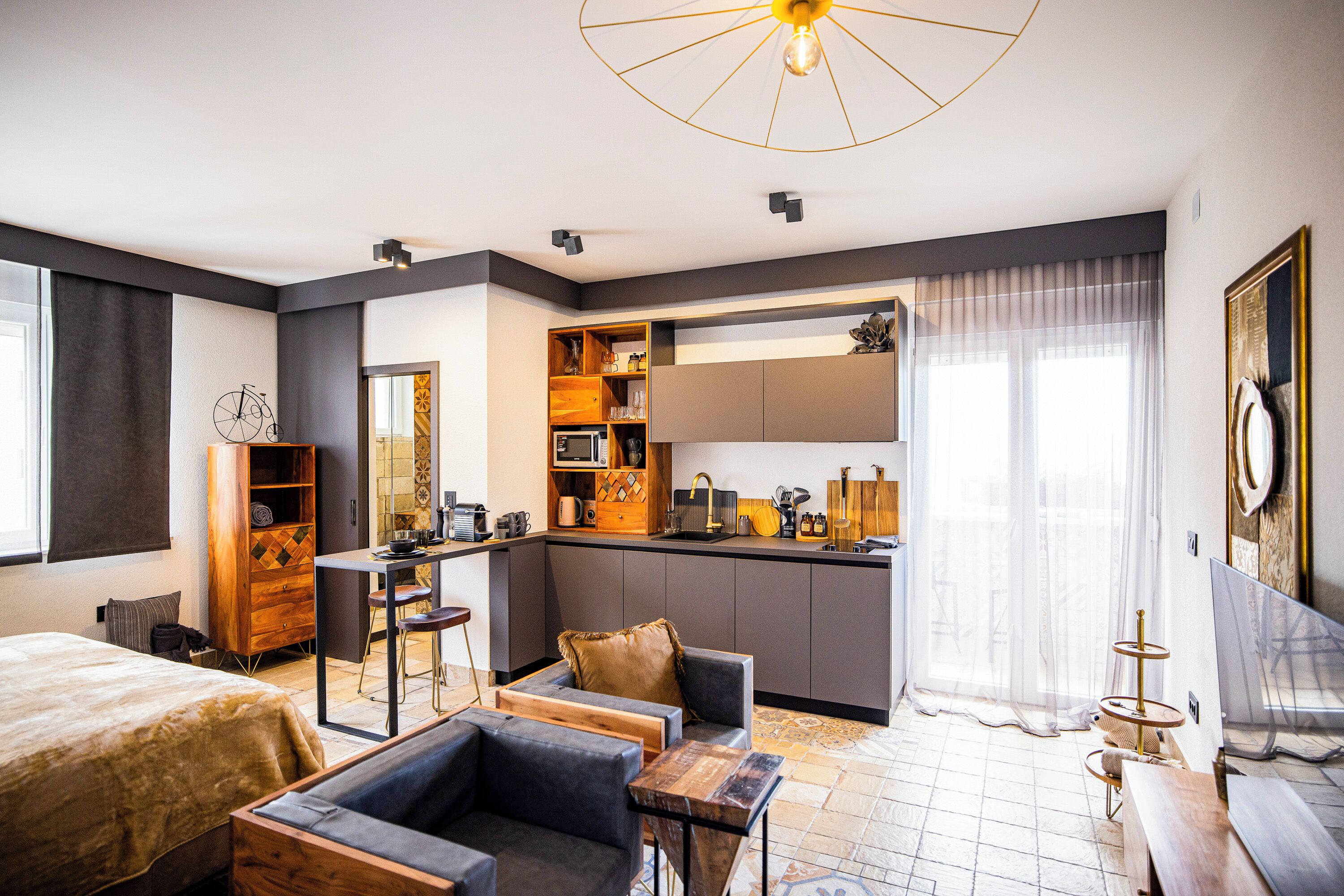 A modern hotel room with a kitchenette, a dining area, and a large bed.
