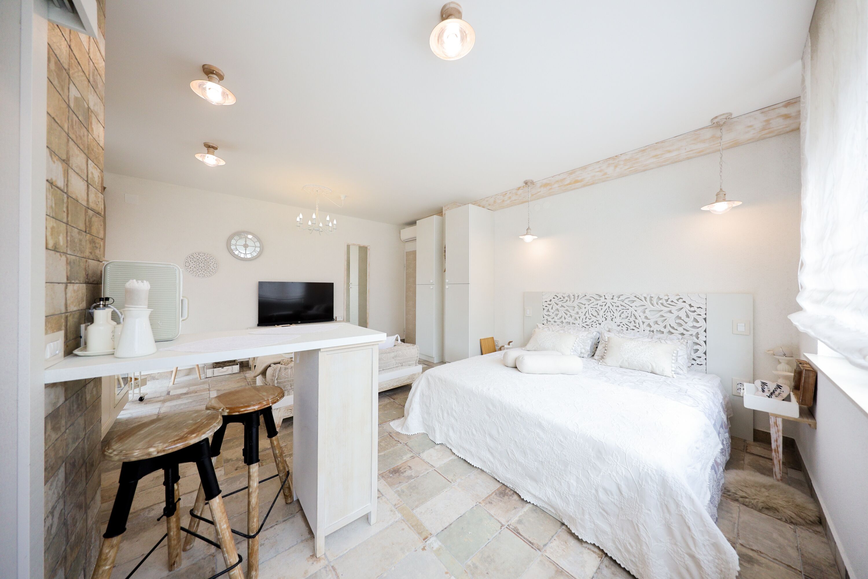 Quarto moderno com cama grande, escrivaninha com banquetas e televisão.