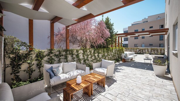 An outdoor patio with a wooden table, white sofas, and a white wall with climbing plants. -  Ika Boutique Luxury Apartments (Zadar)