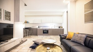 A modern kitchen with white cabinets, a dining area with a black sofa and a round coffee table, and a TV in the living room. -  Ika Boutique Luxury Apartments (Zadar)