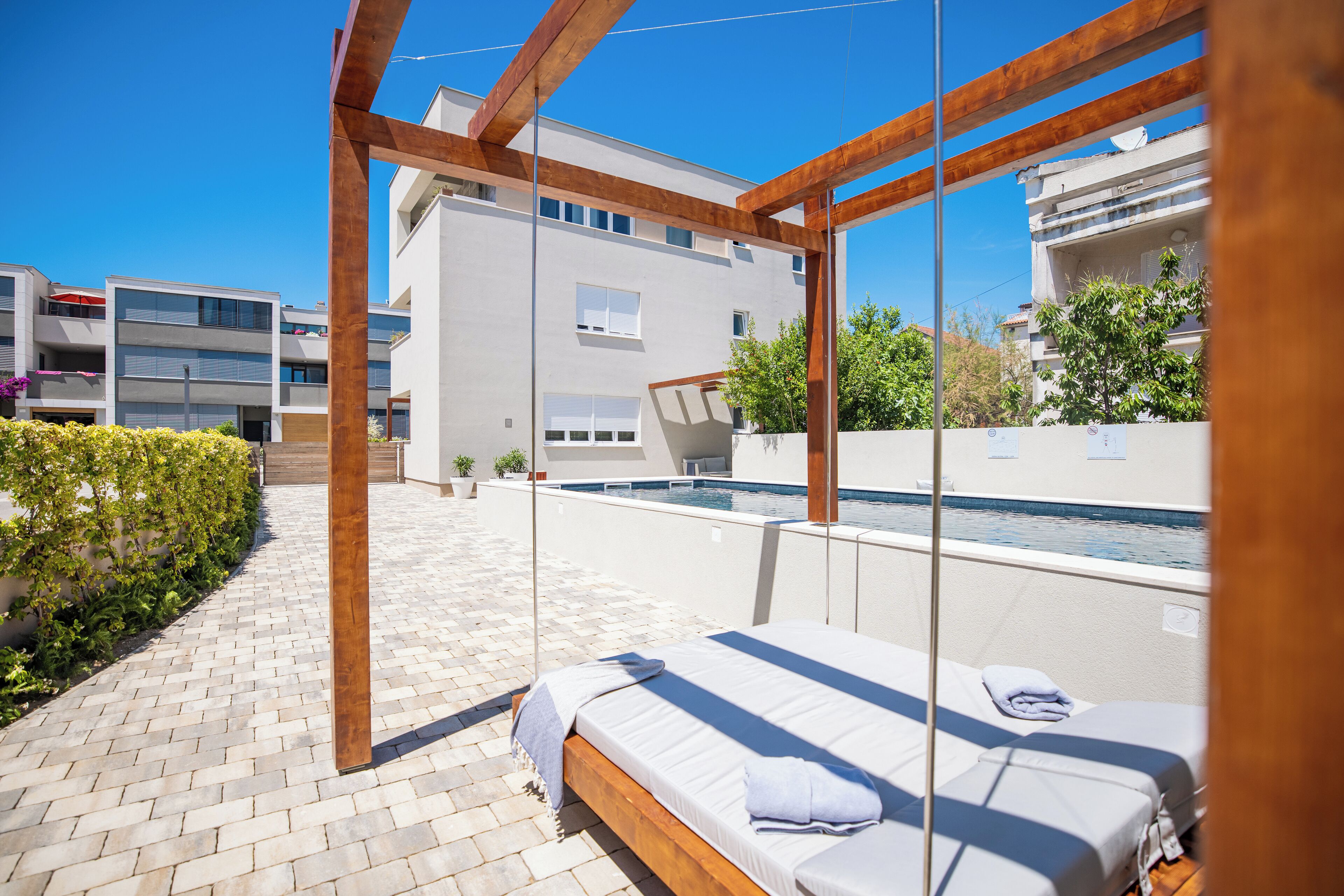Een moderne slaapkamer buiten met een houten pergola, een zwembad en uitzicht op nabijgelegen gebouwen.