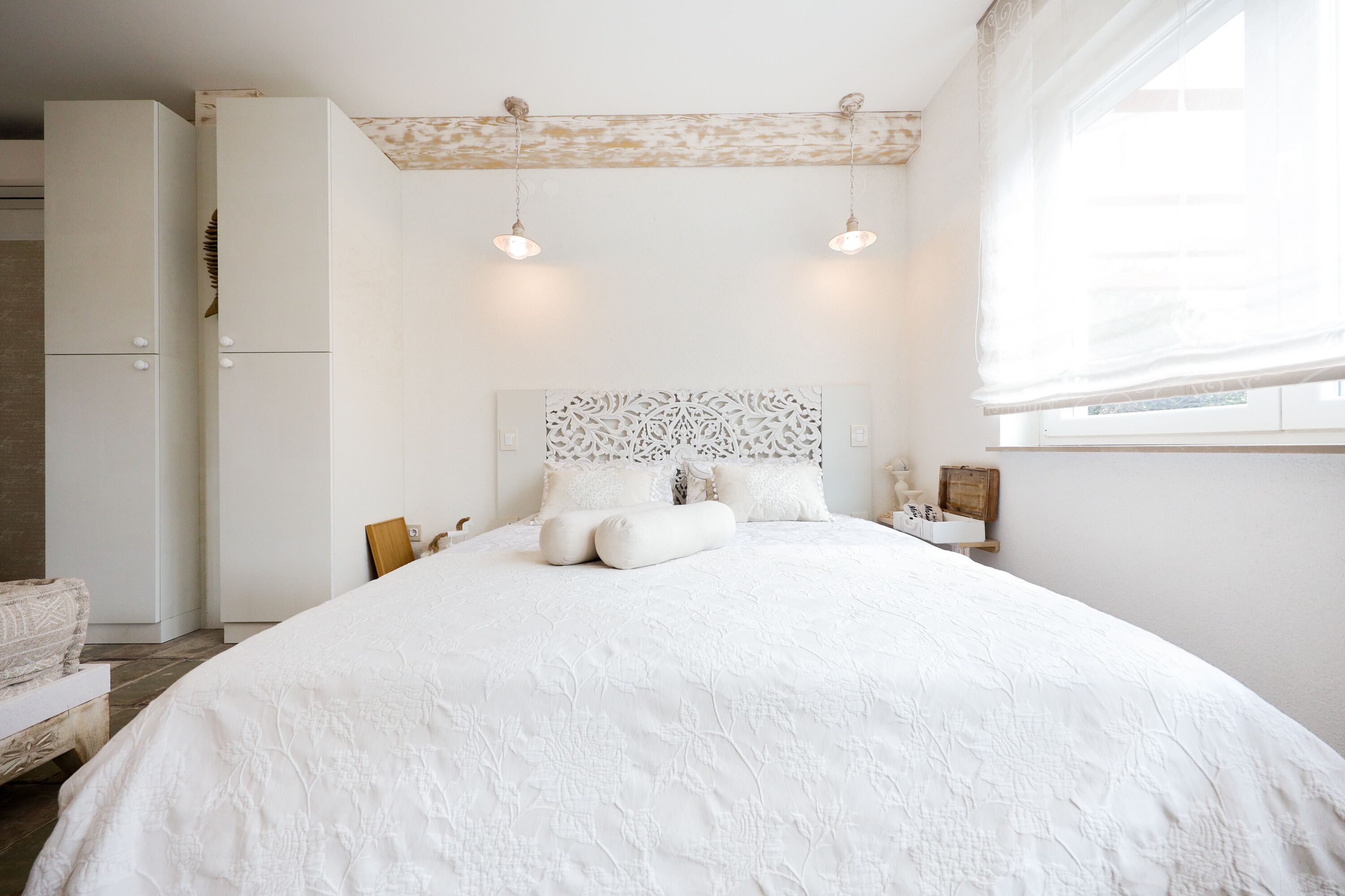 Un letto grande con copripiumino bianco, una testiera decorativa e due abat-jour.