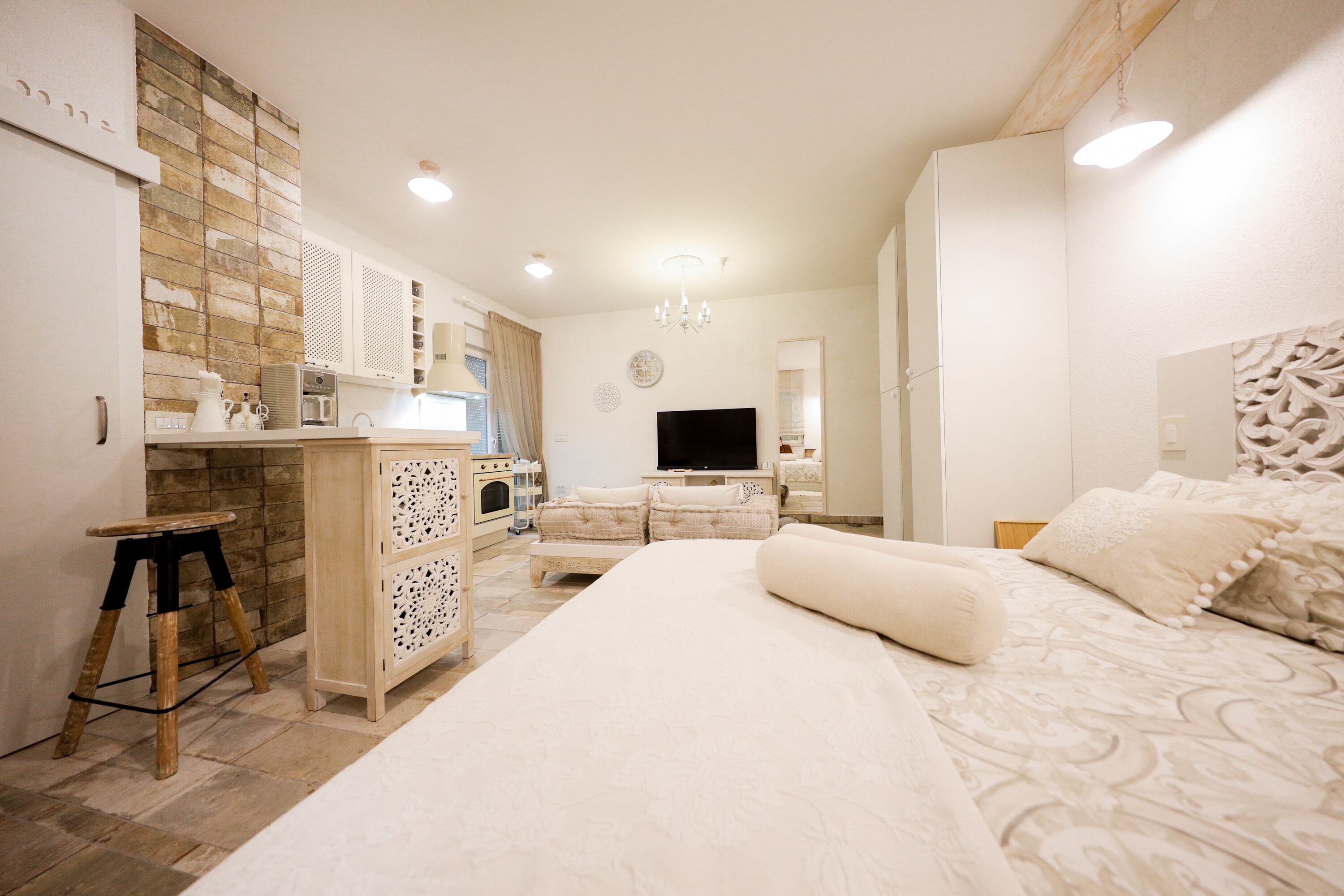 A bedroom with a large bed, a TV, and a kitchenette.