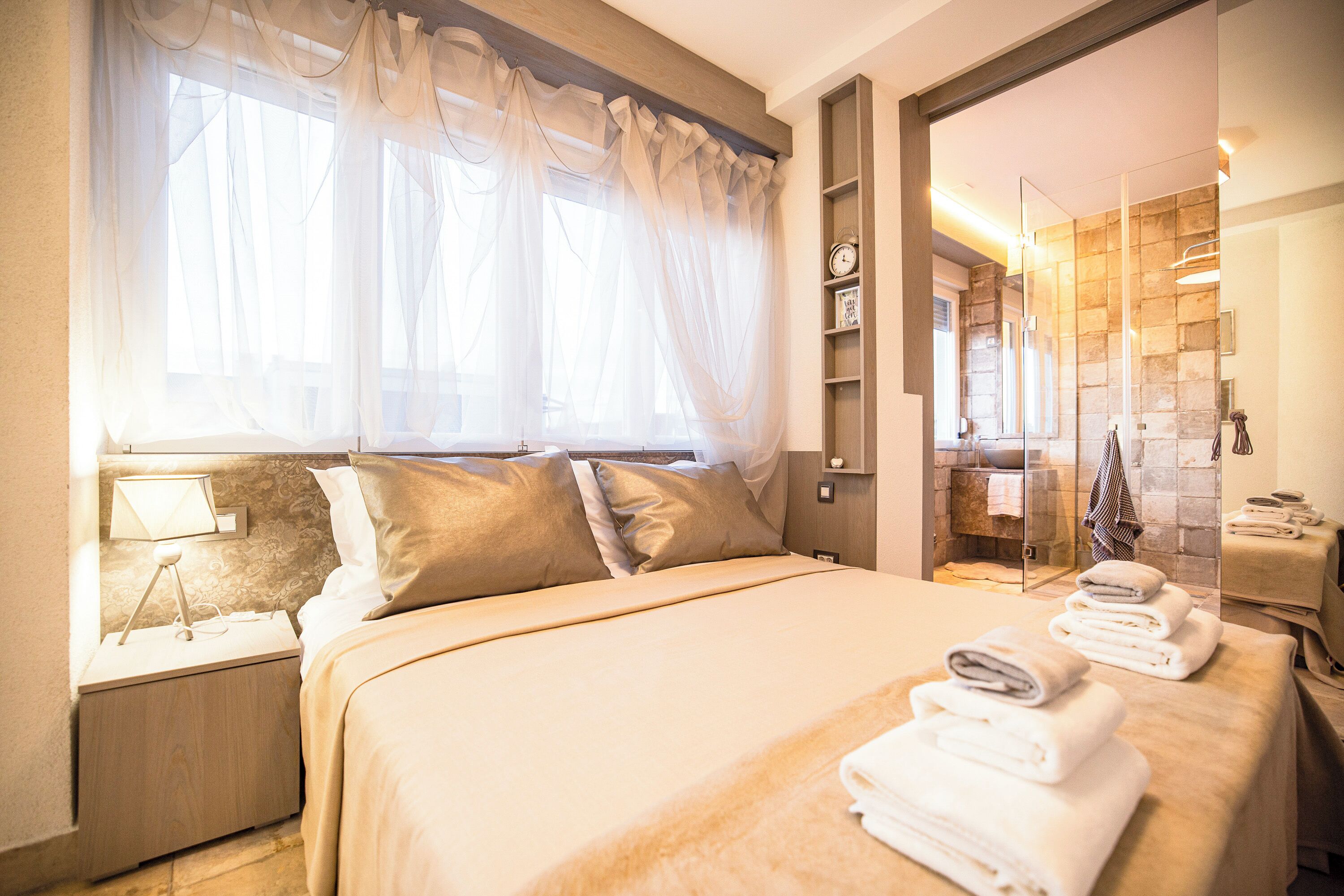A well-lit bedroom with a large bed, a bedside table with a lamp, and a view into the bathroom.