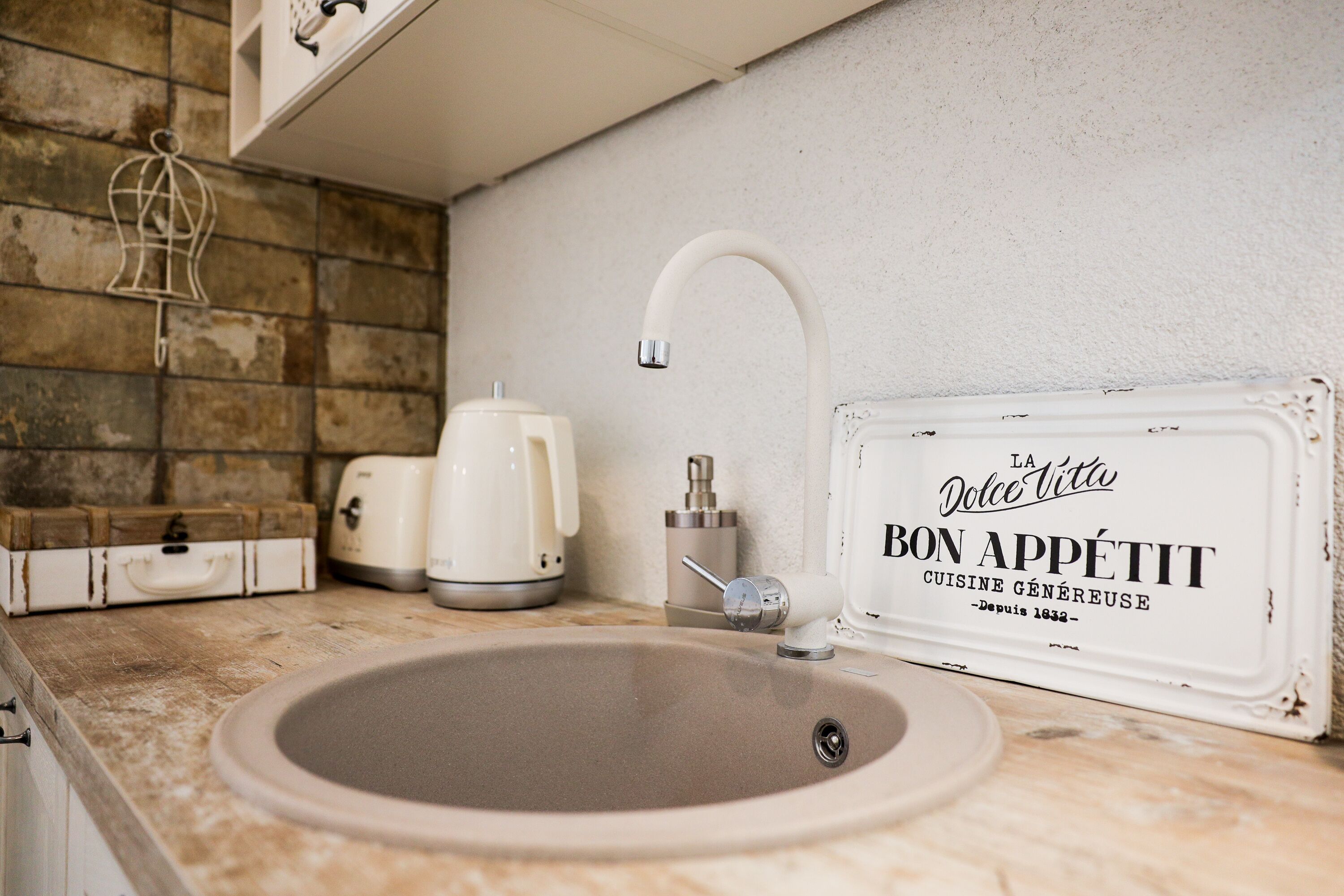 A kitchen sink with a modern faucet, a vintage-style sign, and a coffee maker on the counter.