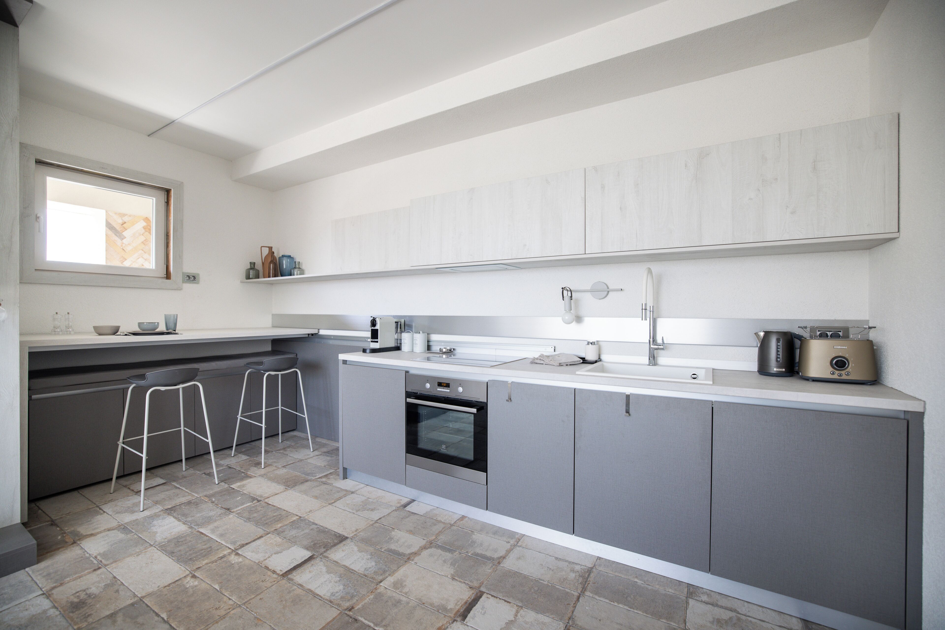 A modern kitchen with grey cabinets, a built-in oven, a sink, and a window above the counter.