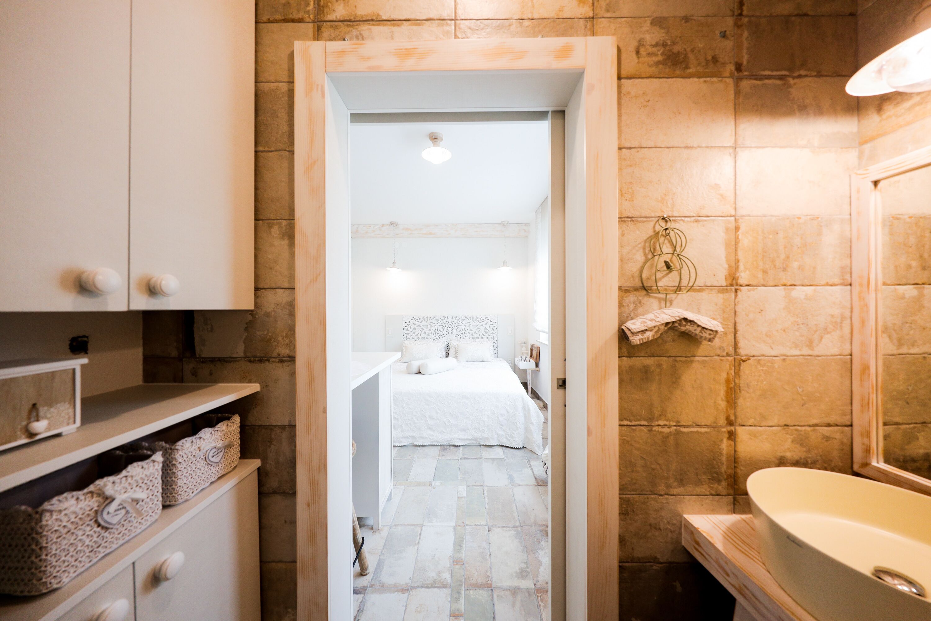 Un baño con bañera, lavabo y ducha. Se ve una cama a través de una puerta abierta al fondo.