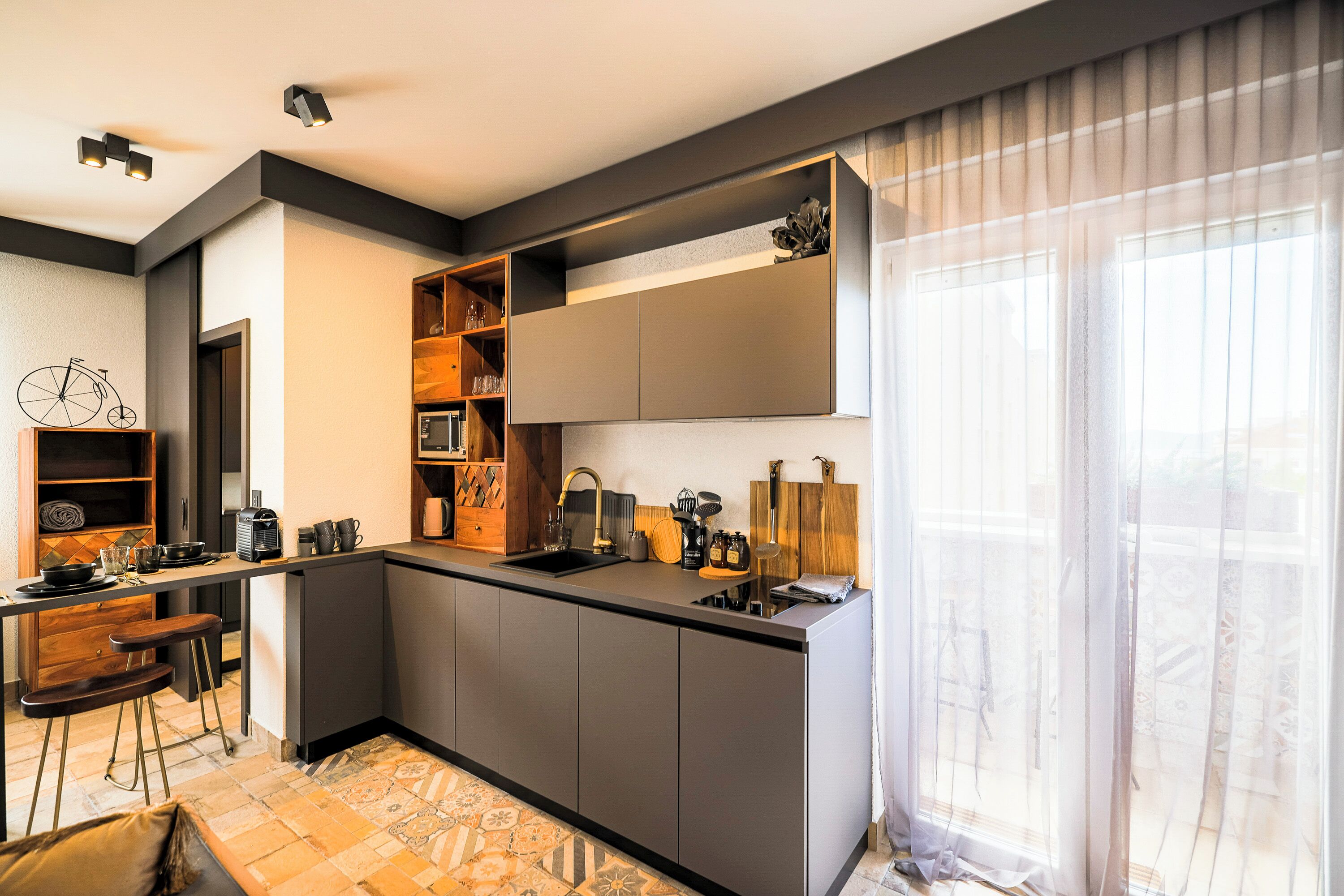 A modern kitchen with a central island, built-in shelves, and a large window with sheer curtains.