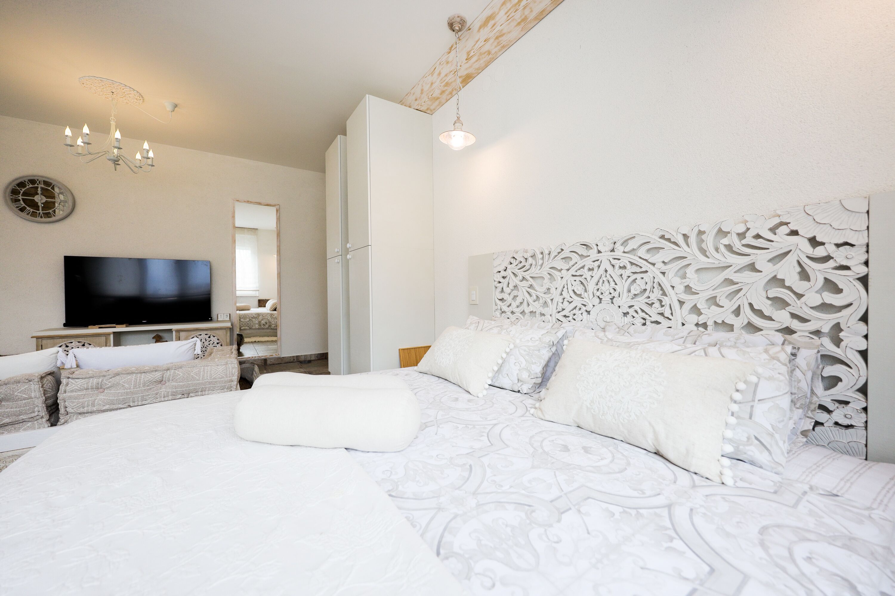 A bedroom with a large bed, a TV, a decorative headboard, and a chandelier.