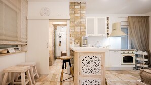A modern kitchen with white cabinetry, a built-in oven, and a dining area with a wooden table and stools. -  Ika Boutique Luxury Apartments (Zadar)