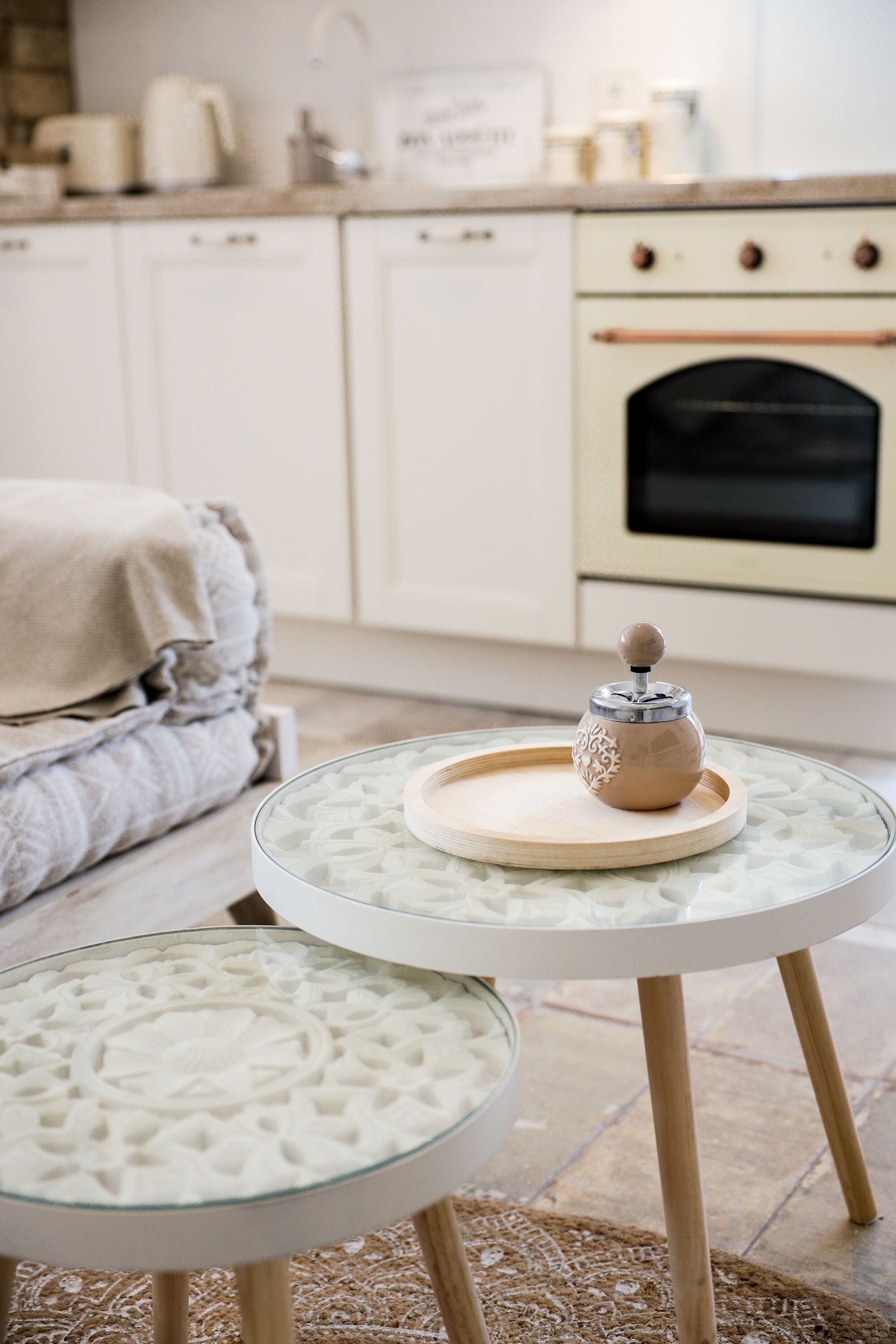 Una cucina con mobili bianchi, un fornello e un tavolo in vetro con un oggetto decorativo.