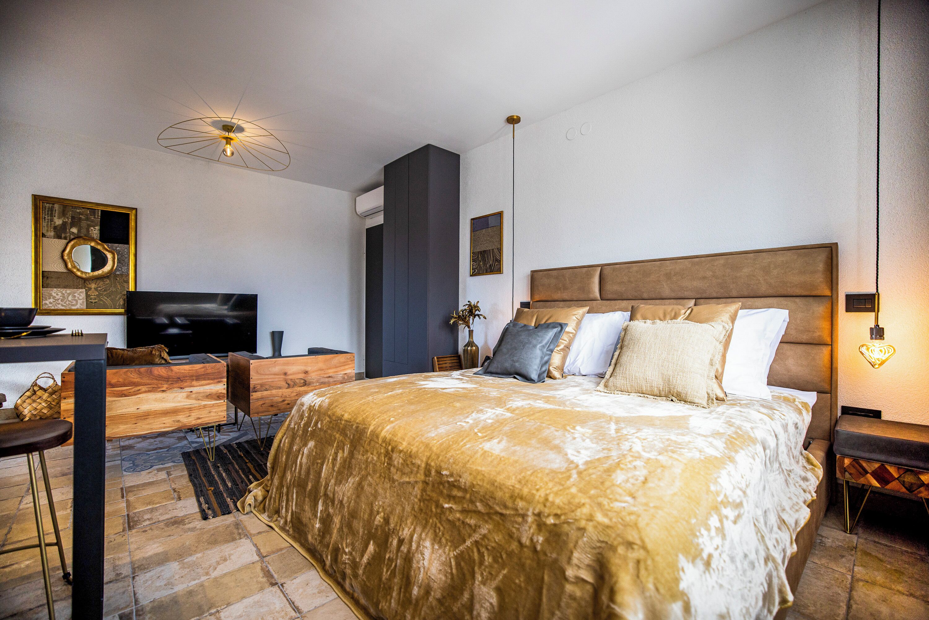 A modern bedroom with a large bed, a TV, a desk, and a unique ceiling light fixture.