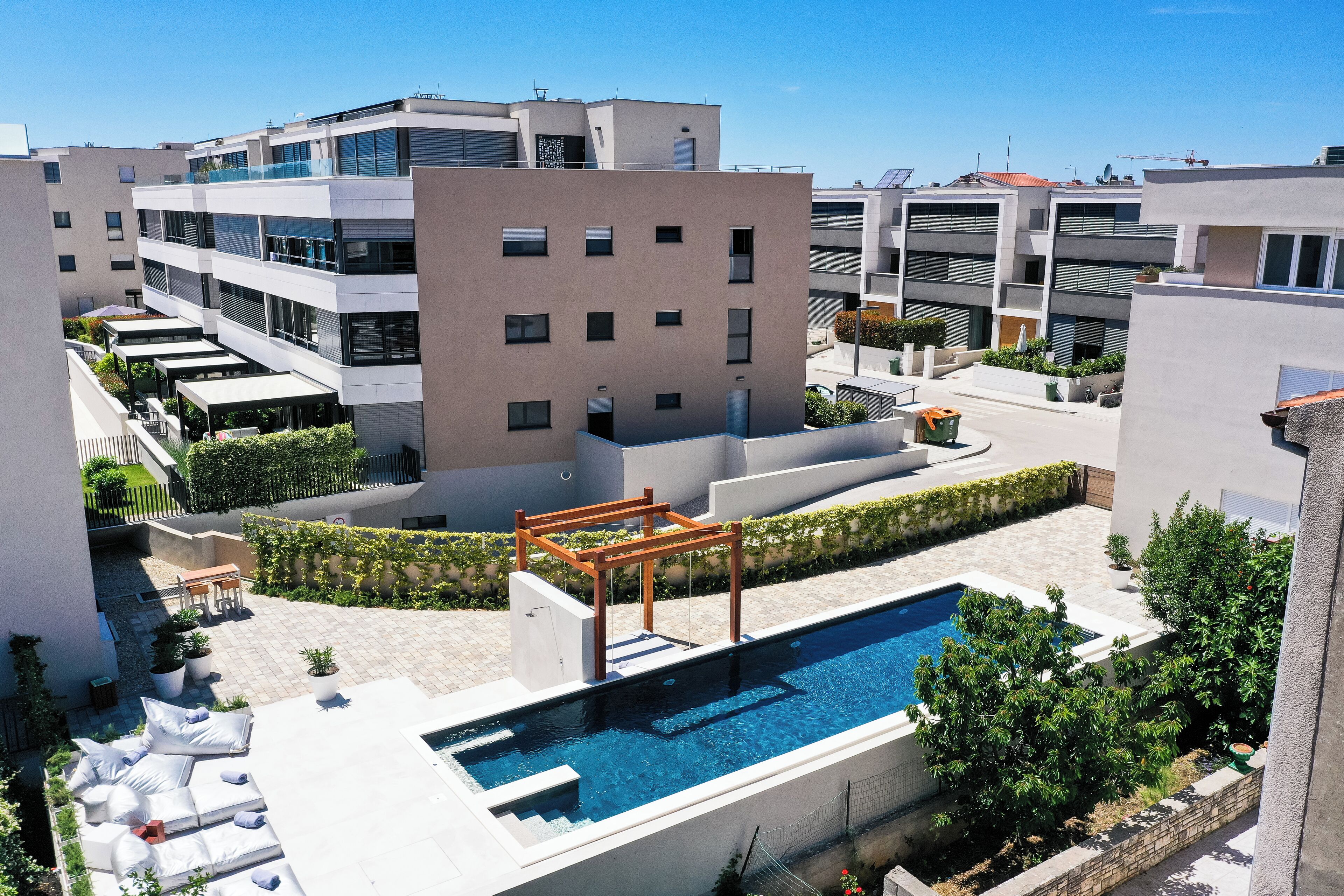 A rooftop pool area with a wooden pergola, lounge chairs, and potted plants.