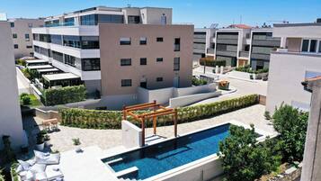 A rooftop pool area with a wooden pergola, lounge chairs, and potted plants.
