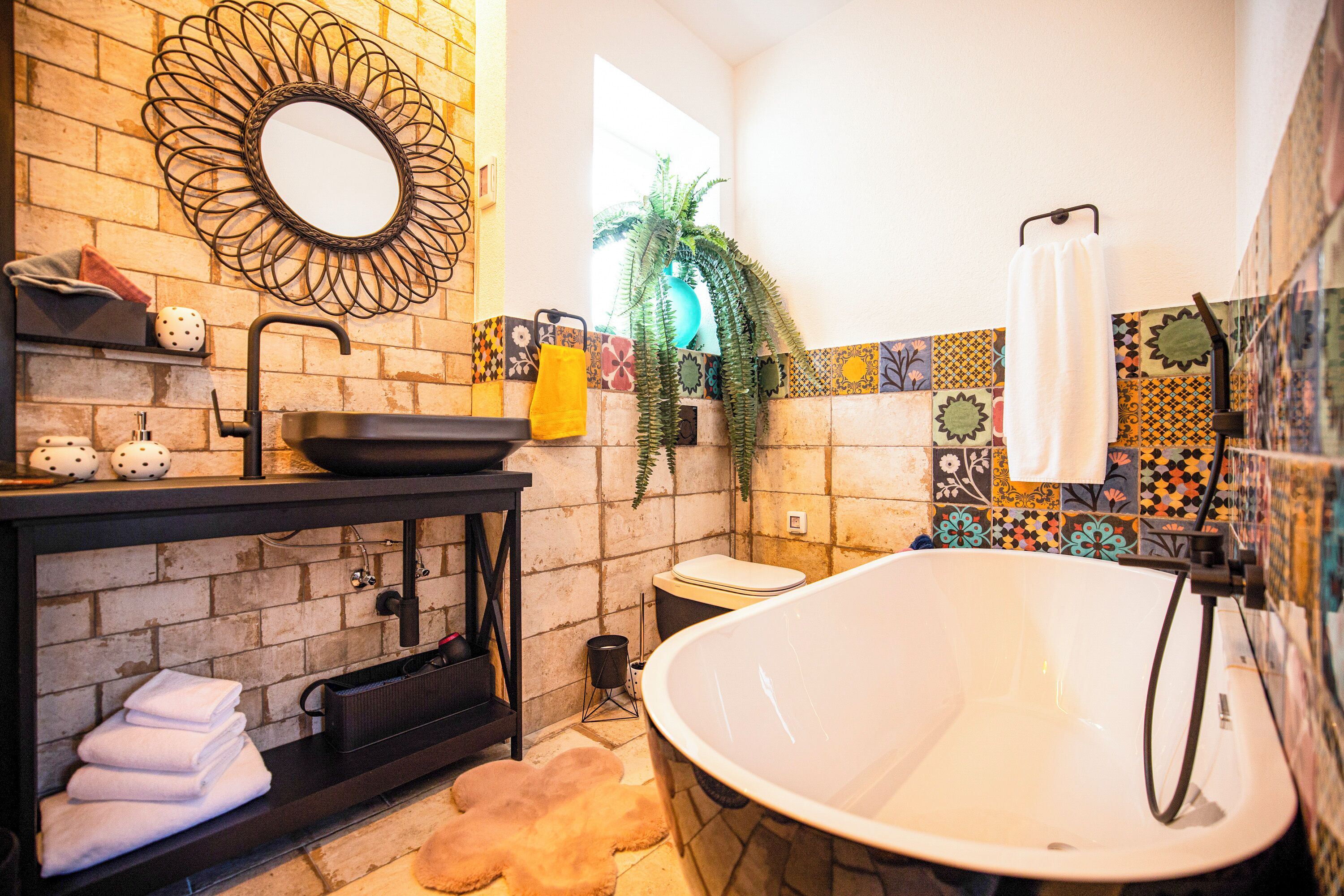 Une salle de bain avec une baignoire sur pieds, un meuble-lavabo noir avec un miroir et un pare-baignoire carrelé.