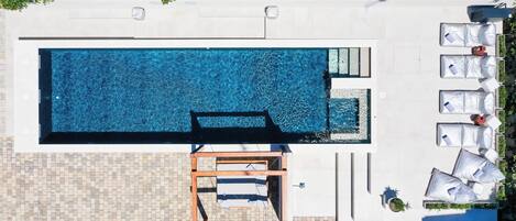 An aerial view of a rectangular swimming pool with a wooden deck and lounge chairs.