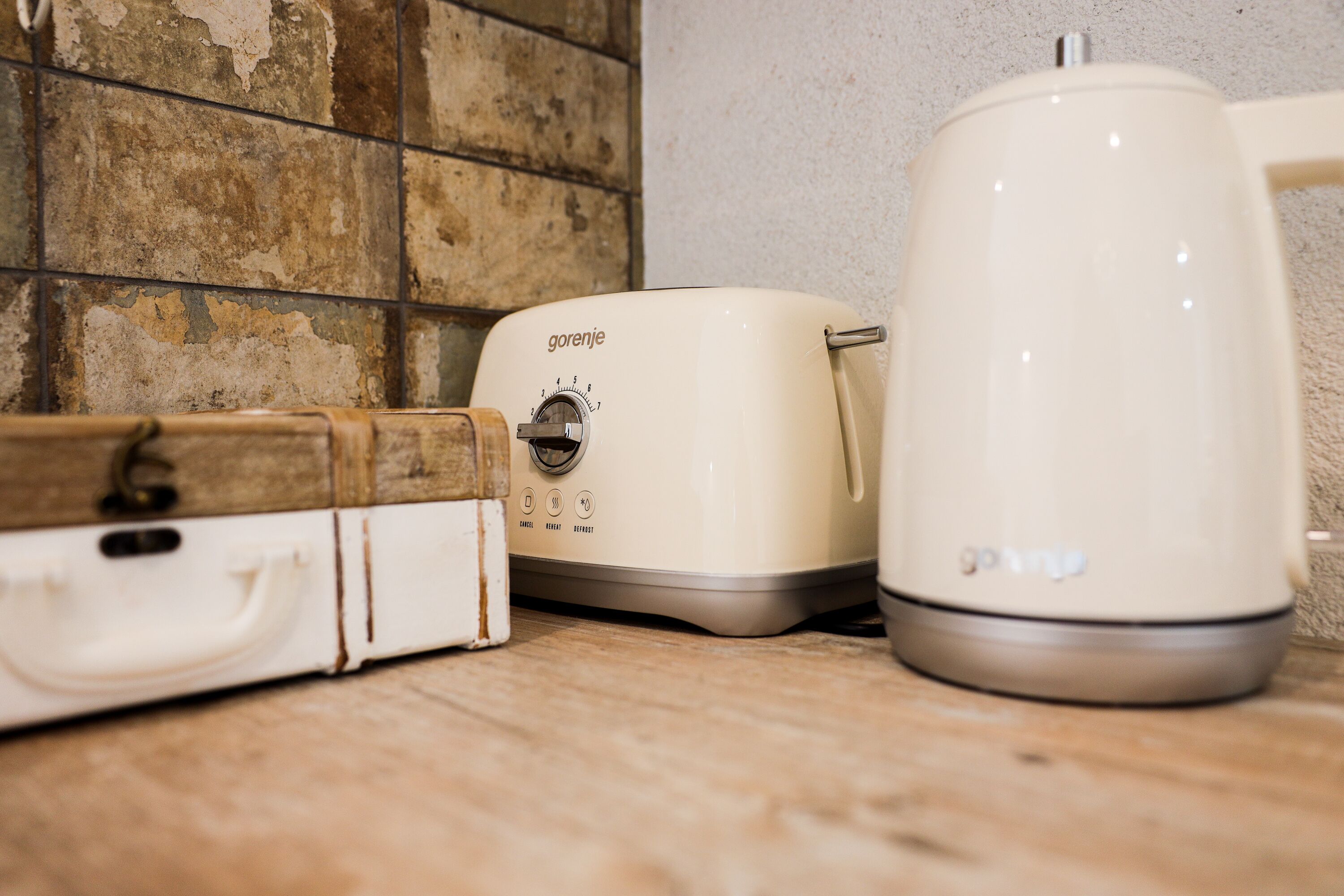Eine Küche mit einem weißen Wasserkocher, einem Toaster und einer Holzschatulle auf der Arbeitsfläche.