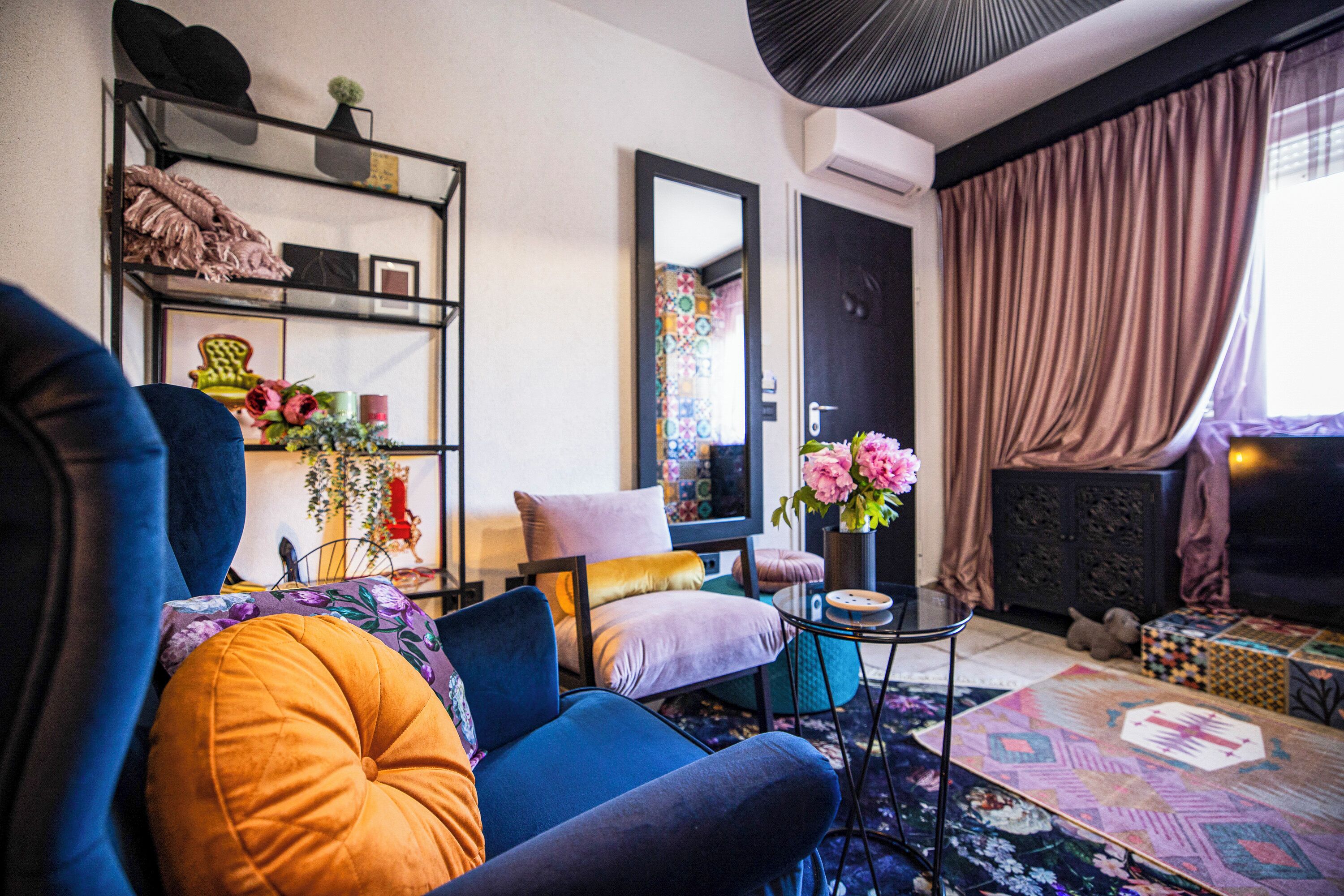 A modern living room with a sofa, armchair, and a small coffee table. There is a bookshelf with decorative items and a mirror.