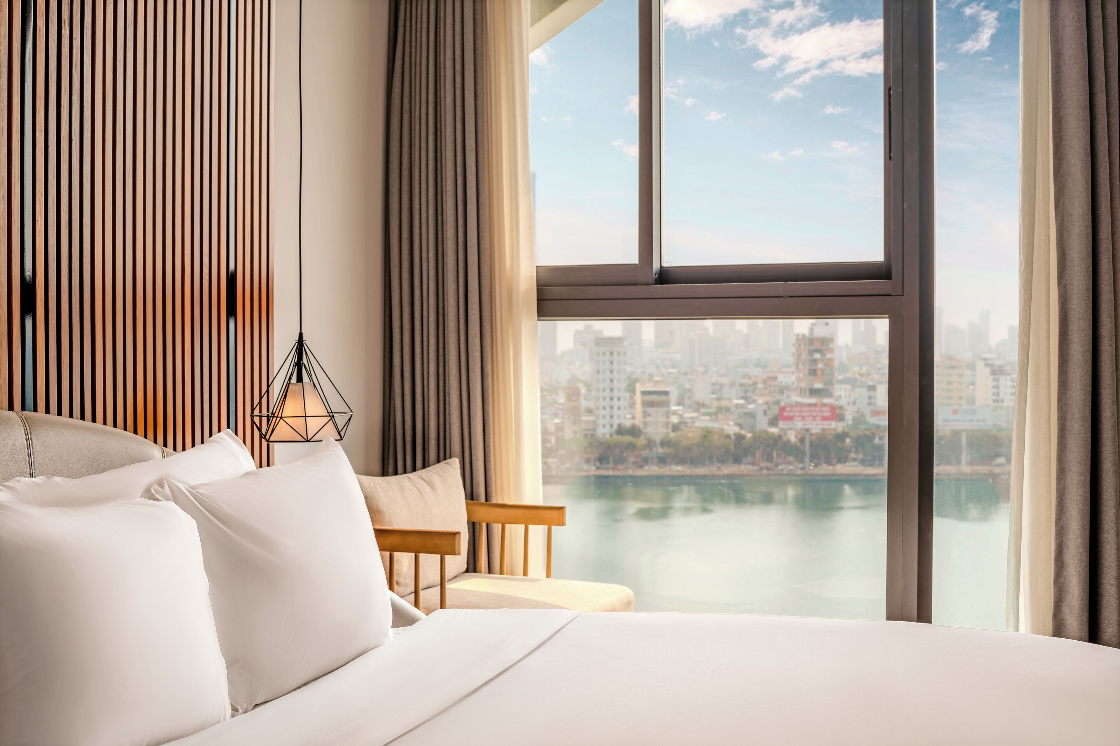 Camera d'albergo con un letto grande, vista sulla città attraverso una finestra e sullo skyline urbano in lontananza.