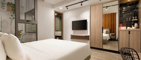 A modern hotel room with a large bed, a flat-screen TV, a wooden wardrobe, and a small kitchenette.