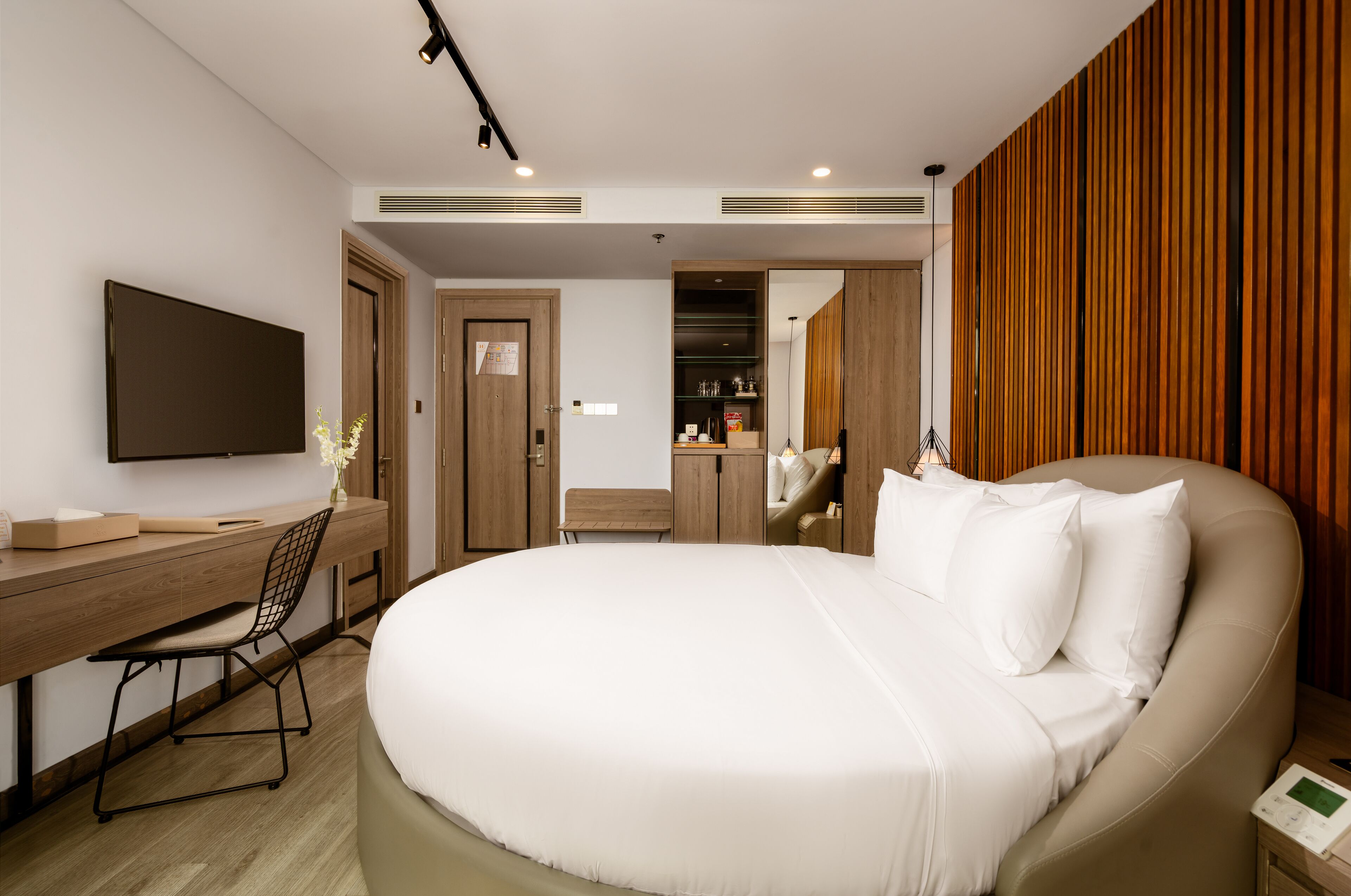Habitació d'hotel moderna amb un llit gran, un escriptori amb una cadira, una televisió de pantalla plana i un mur amb panells de fusta.