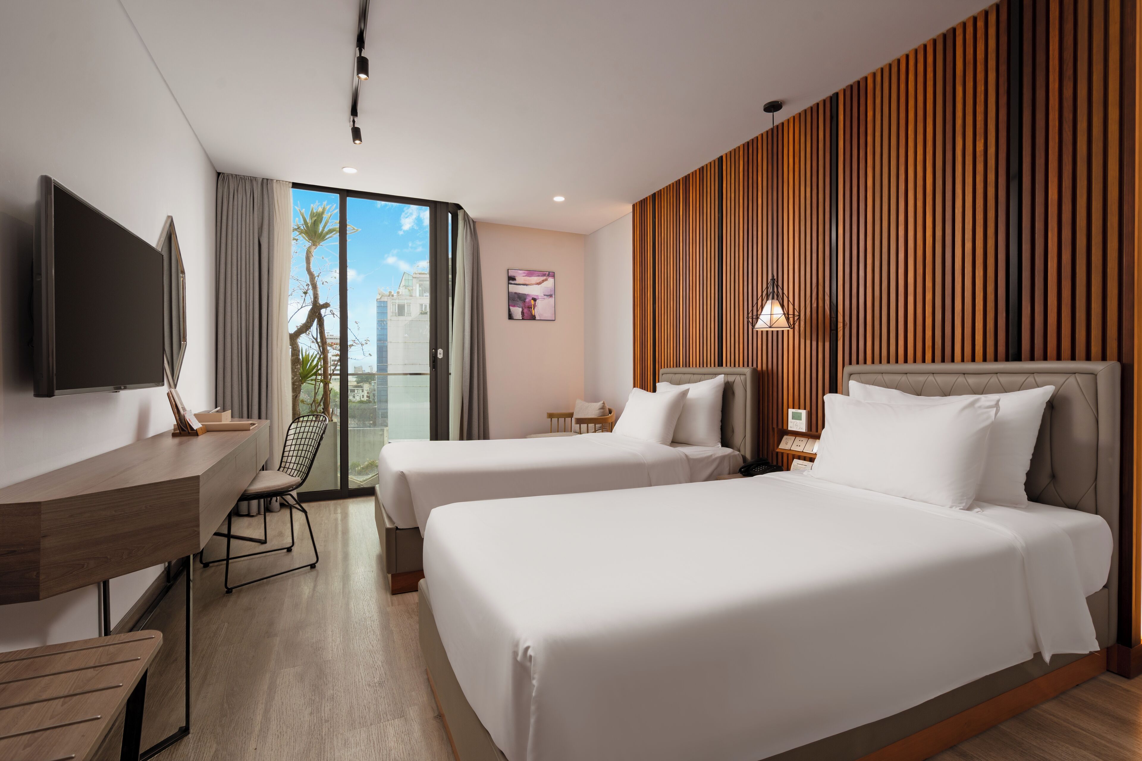 A hotel room with two beds, a desk, a chair, and a TV.