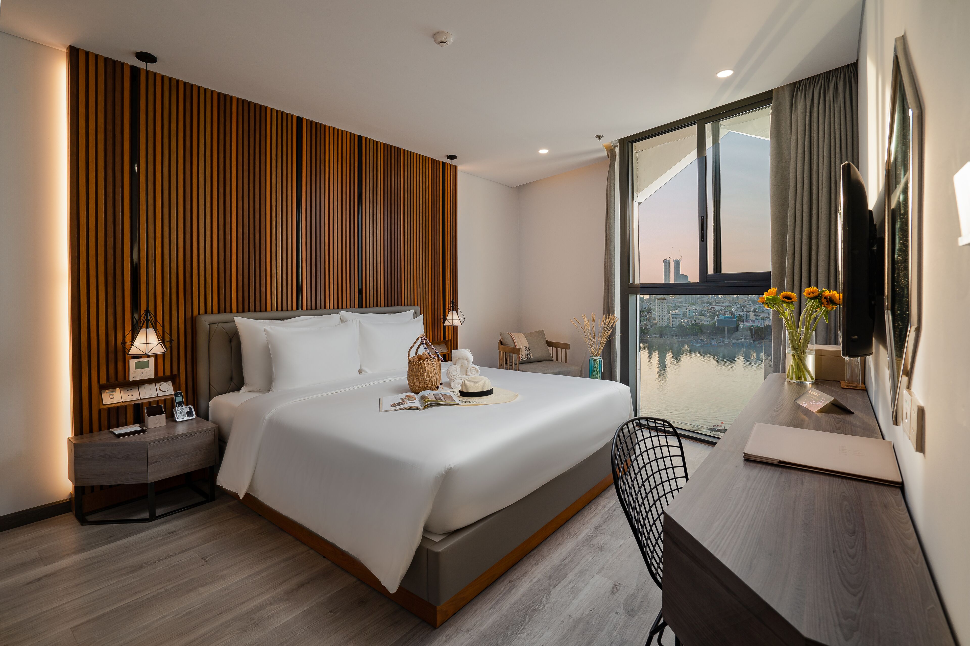 Habitación de hotel moderna con una cama grande, un escritorio y vistas de un paisaje urbano a través de un ventanal.