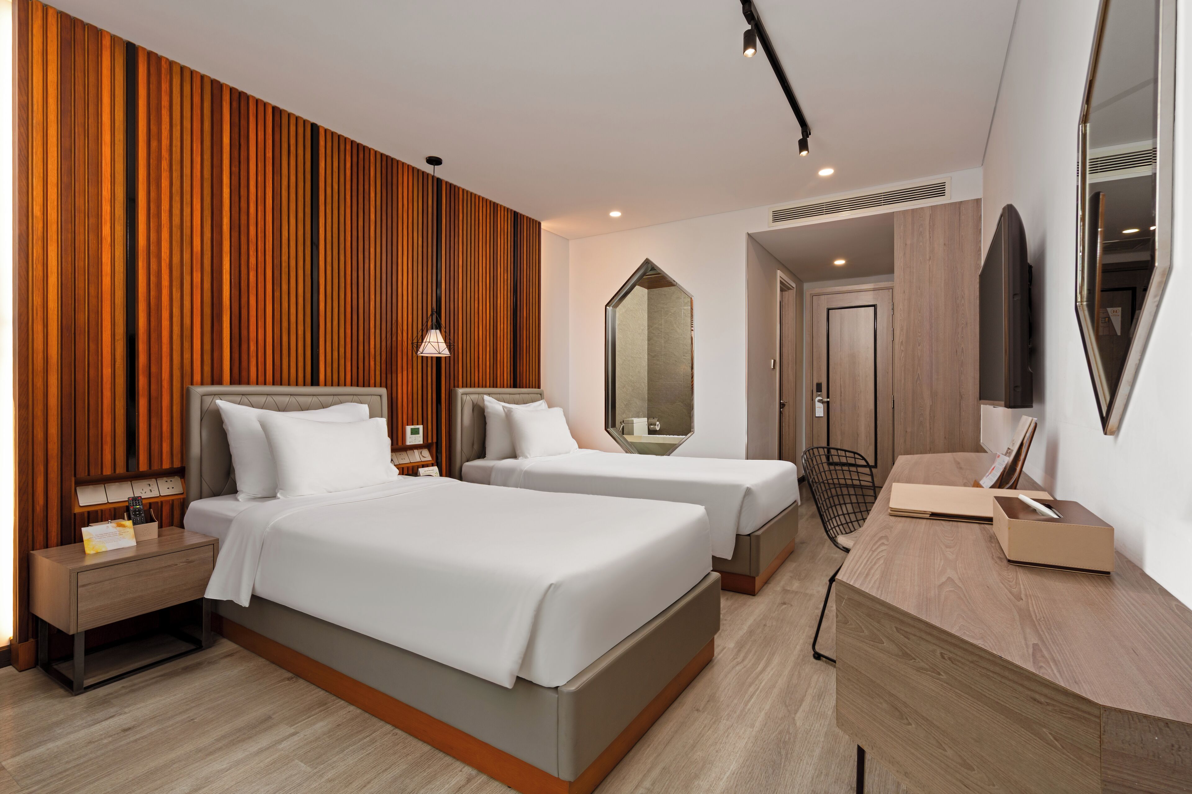 A hotel room with two beds, a wooden accent wall, a large mirror, a desk, and a TV.
