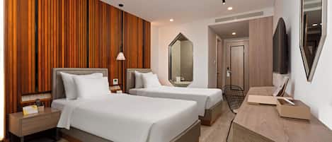 A hotel room with two beds, a wooden accent wall, a large mirror, a desk, and a TV.