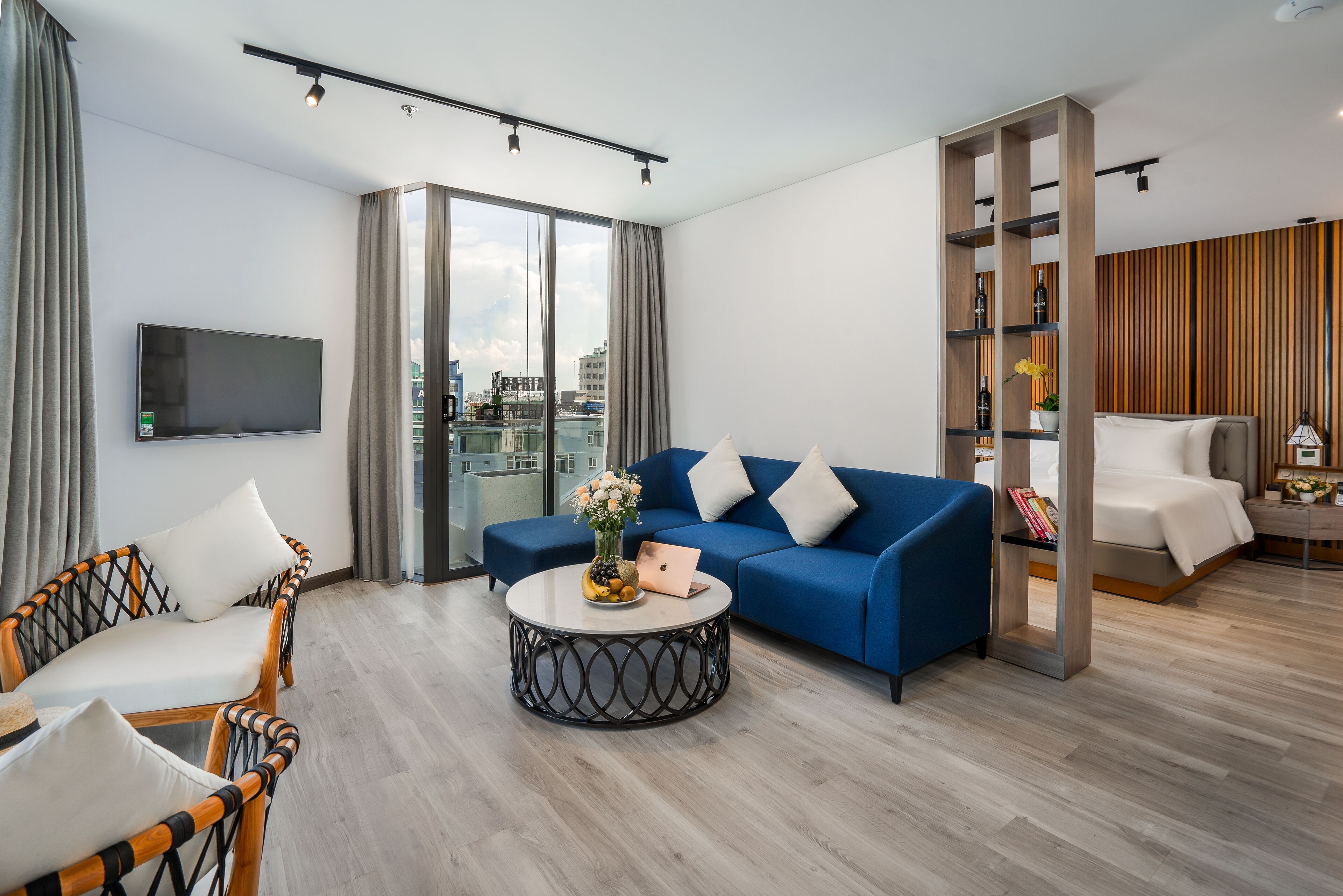 A modern living room with a blue sofa, a round coffee table with a vase, and a flat-screen TV mounted on the wall.