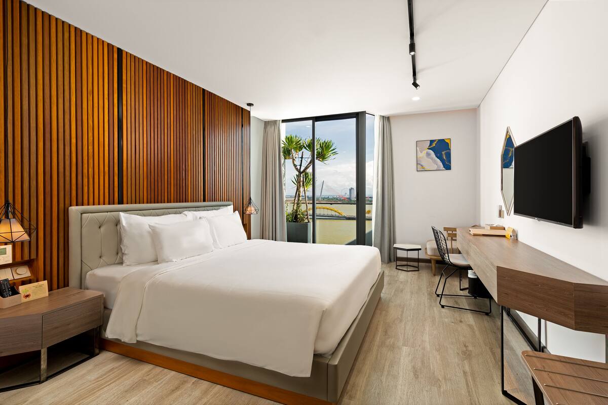 Quarto de hotel moderno com uma cama grande, uma escrivaninha e uma televisão.