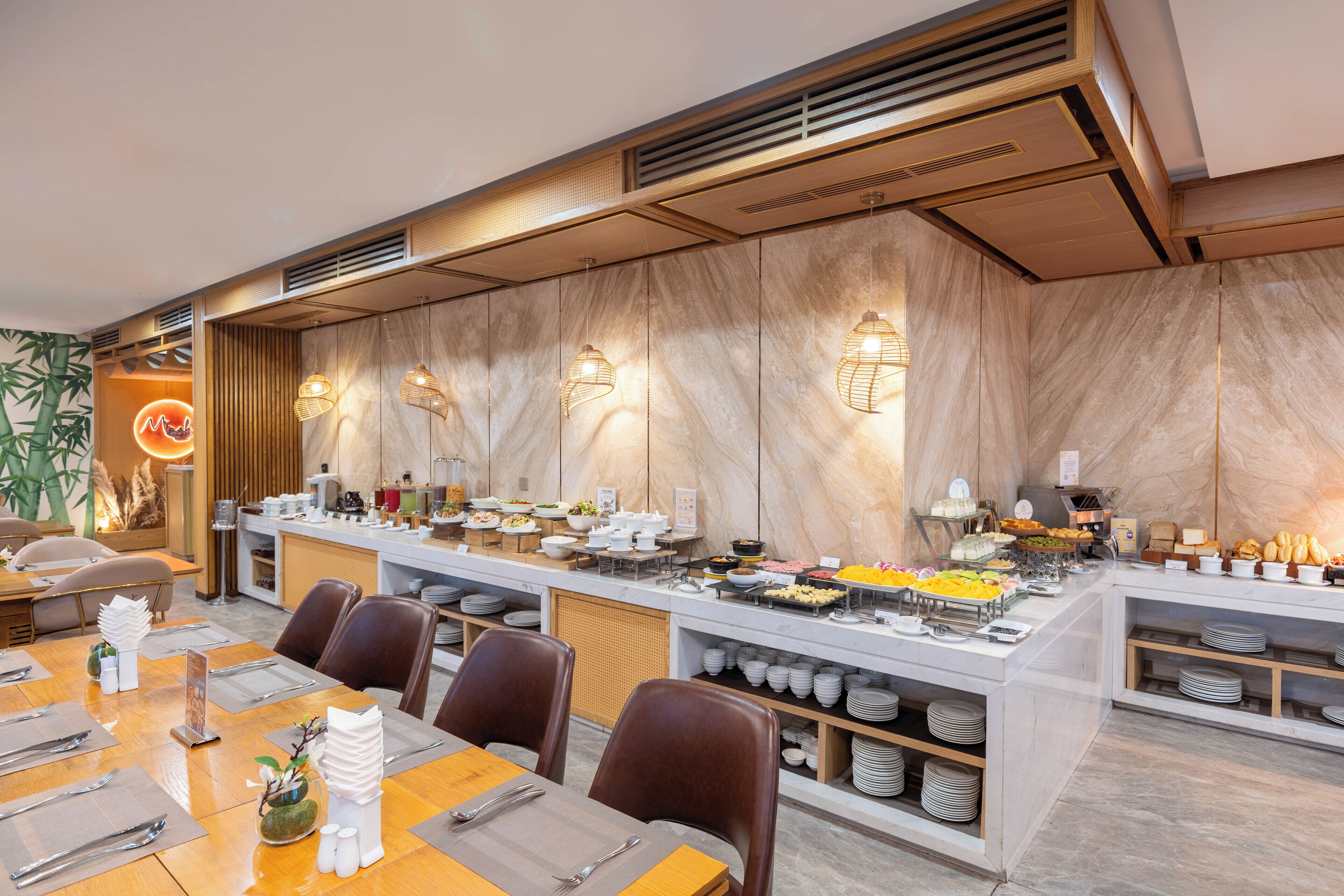 A buffet setup with various food items, a seating area with tables and chairs, and a decorative wall with a neon sign.