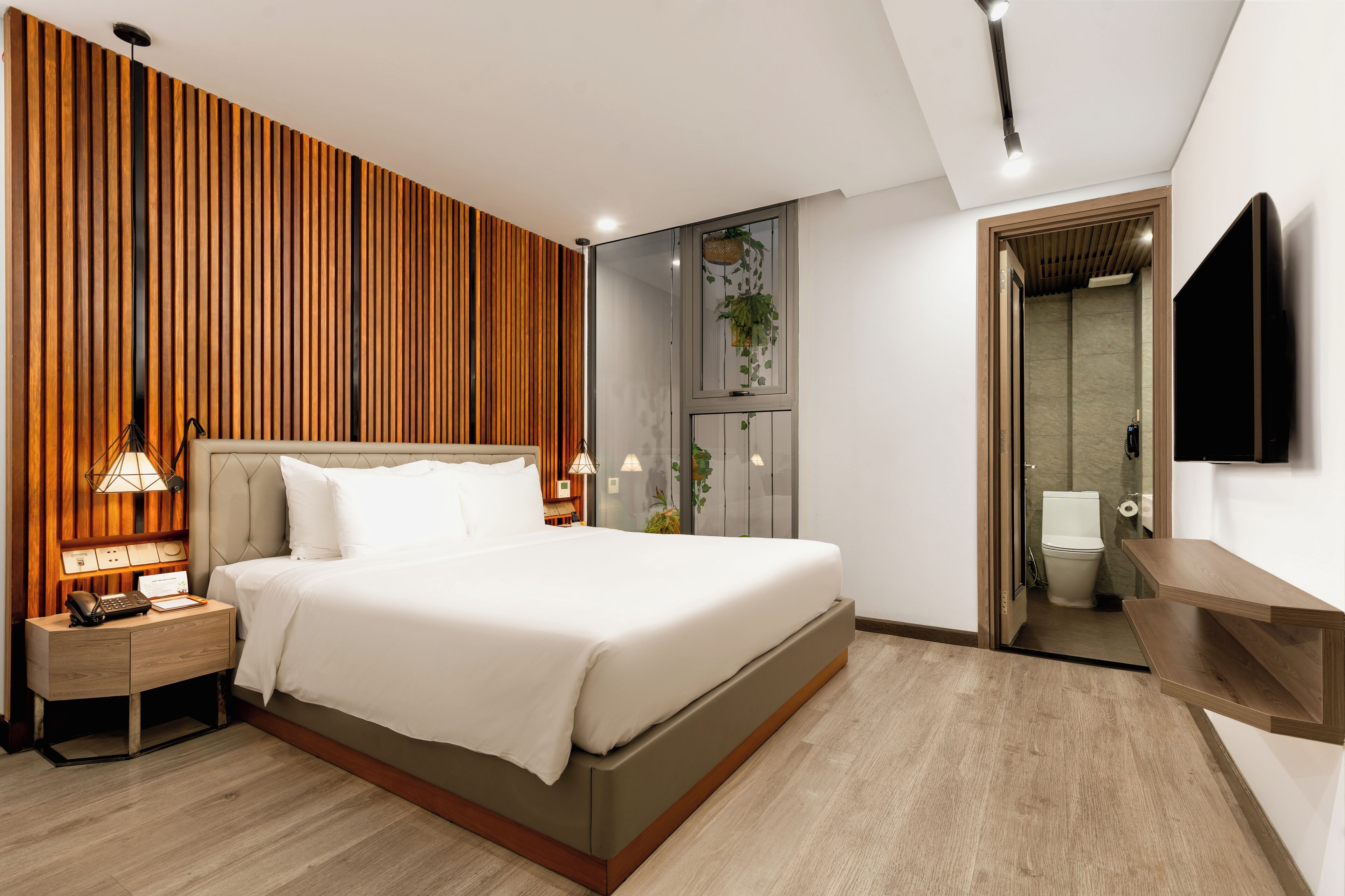 Un dormitorio moderno con una cama grande, lámparas de noche, un cabecero de madera y un televisor montado en la pared.