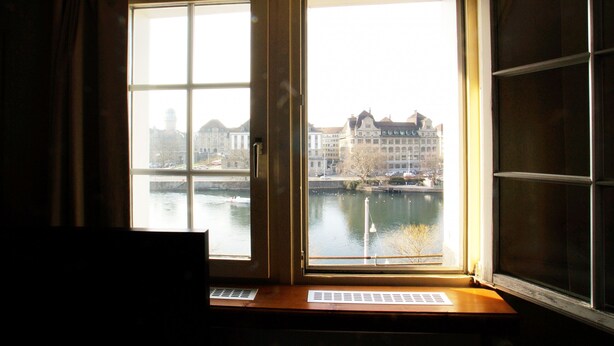 A room with a large window overlooking a river and buildings. - ZH Niederdorf II - Hitrental Apartment (Zürich)