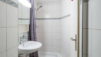 Une salle de bain avec un lavabo blanc, une douche avec un rideau violet et des murs carrelés.