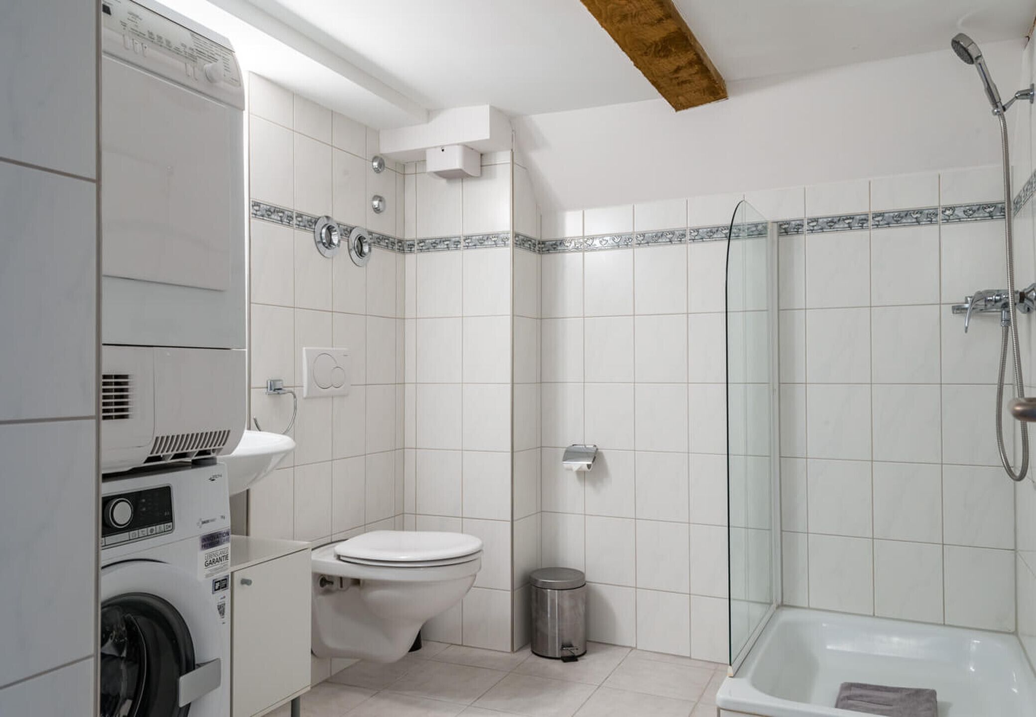 A compact bathroom with a washing machine, toilet, and a glass-enclosed shower area.