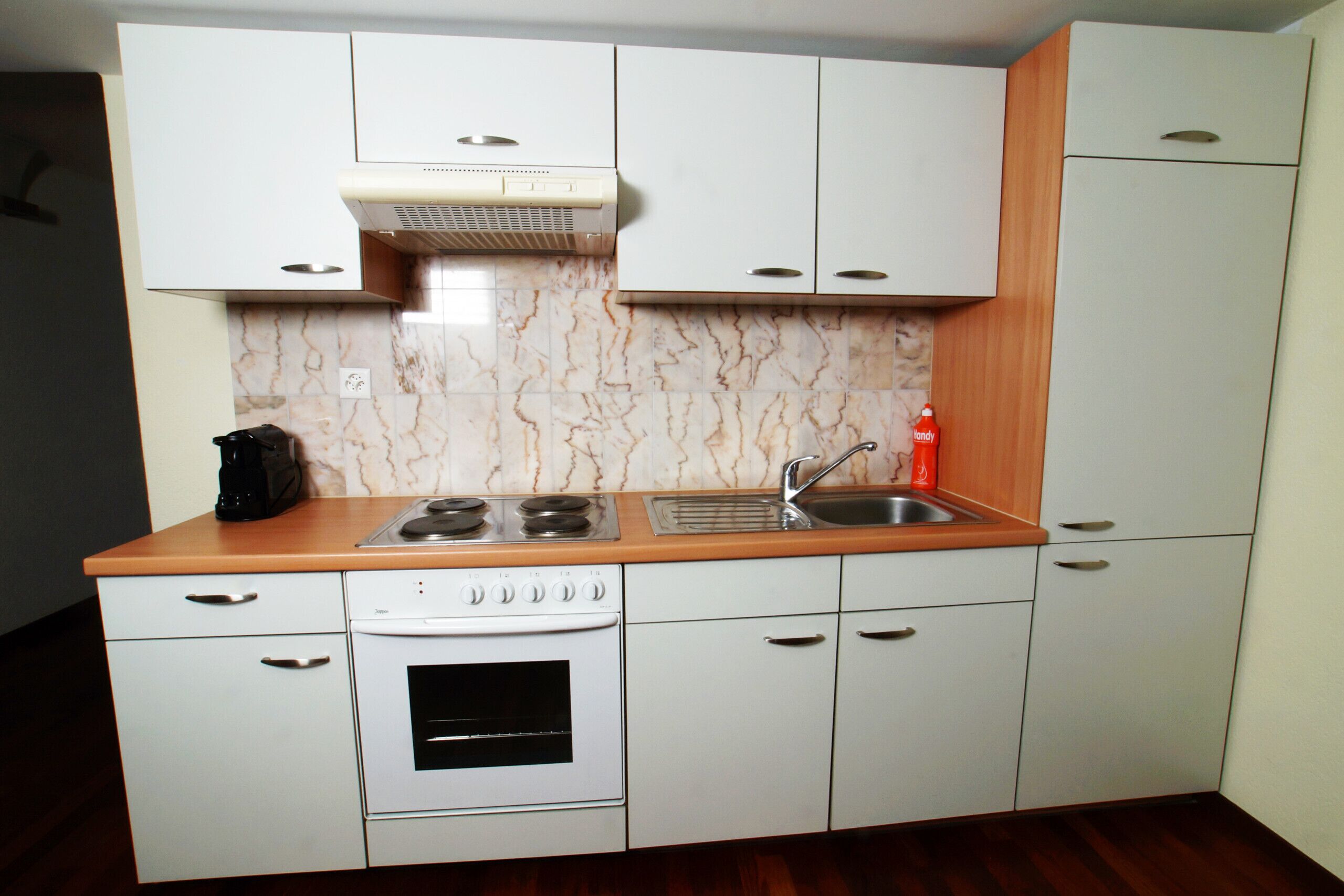 A compact kitchen with white cabinets, a built-in oven, a stove, and a sink.