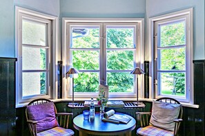 Een erker met drie ruiten, een tafel met stoelen en een lamp.