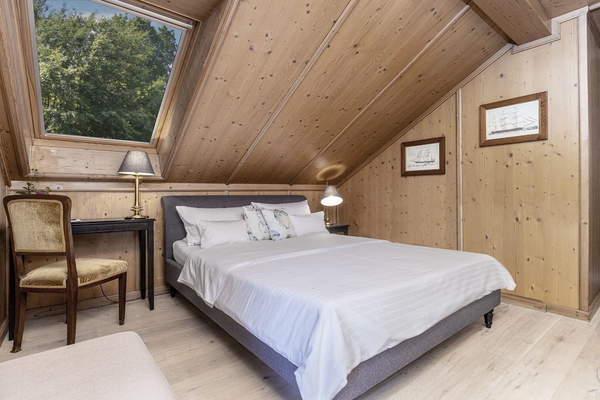 Une chambre à coucher comprenant un lit, un bureau, une chaise et une fenêtre donnant sur des arbres.