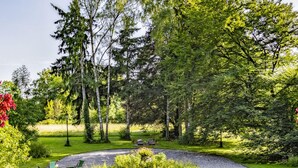 Ein Garten mit einem gepflasterten Weg, der zu einem kreisförmigen Blumenbeet inmitten verschiedener Pflanzen und Bäume führt.