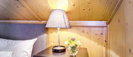 A wooden cabin room with a bed, a nightstand with a lamp, and a vase with flowers.