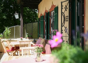 Een buitenruimte met houten meubels en een tafel, omgeven door een tuin met planten en bloemen in potten.