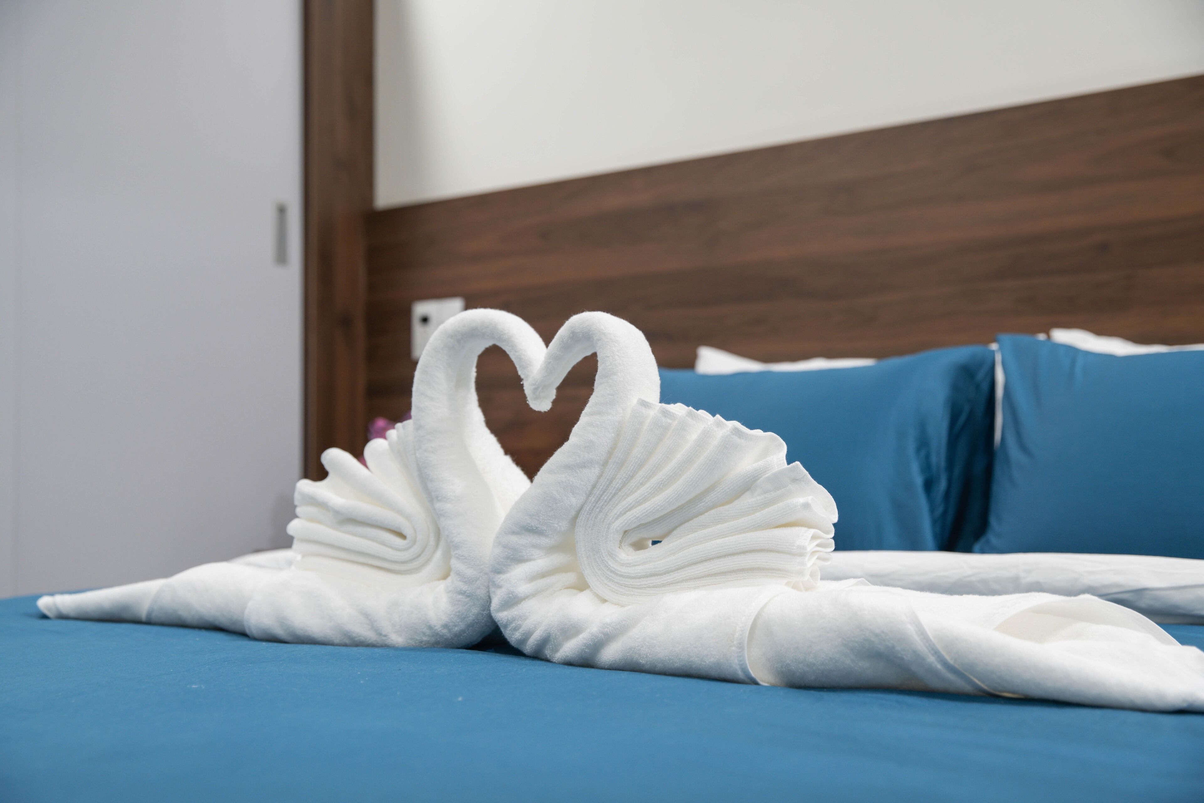 A bed with a blue bedspread and two white towels arranged in the shape of swans.