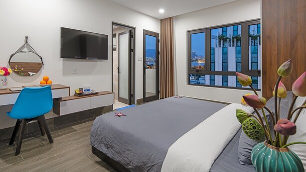 Una habitación de hotel moderna con cama, escritorio, silla, televisor y un ventanal con vistas a la ciudad.