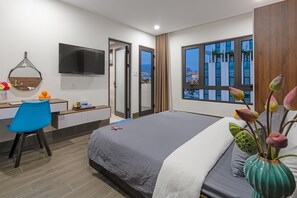 Una habitación de hotel moderna con cama, escritorio, silla, televisor y un ventanal con vistas a la ciudad.