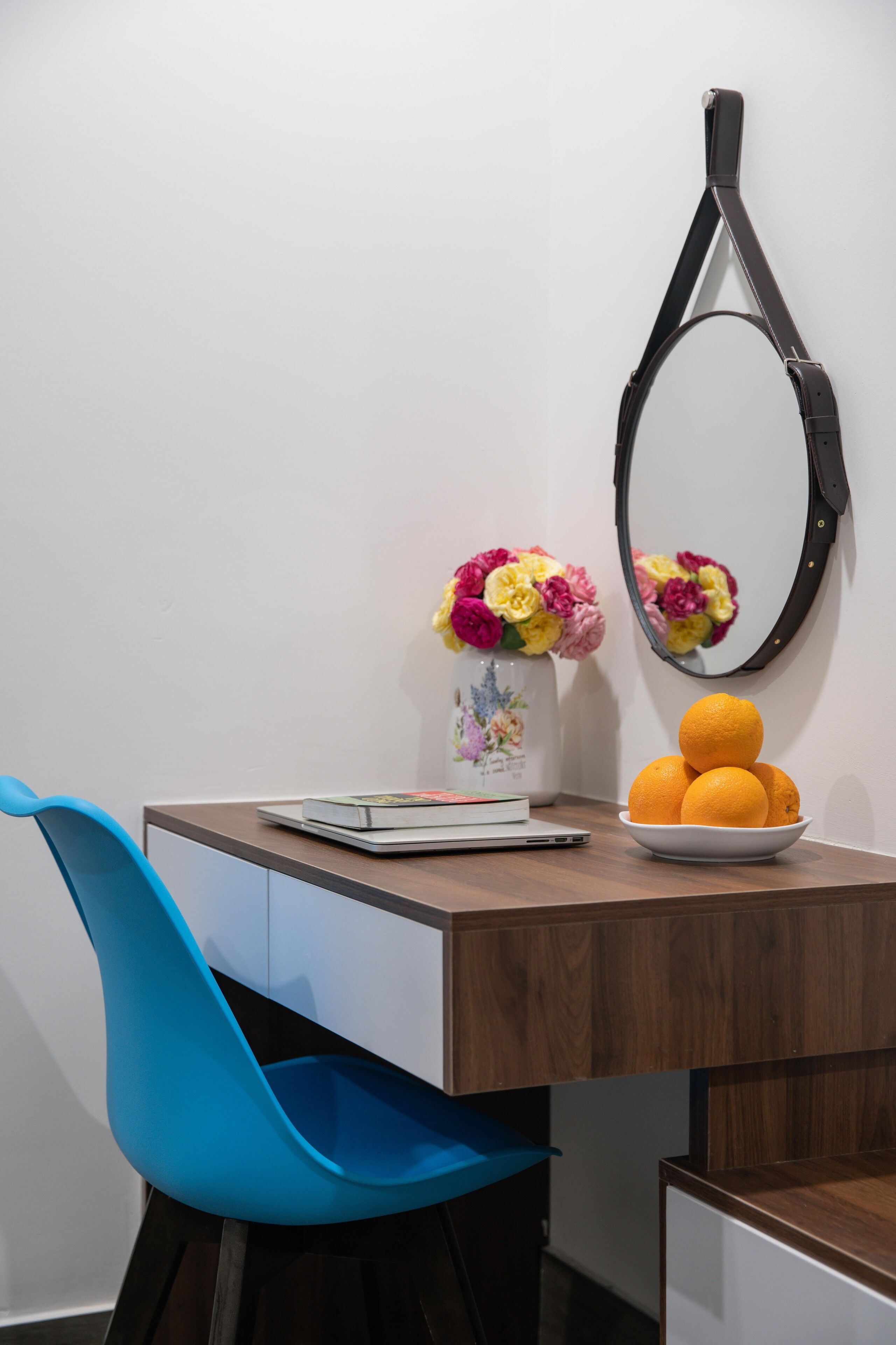 A desk with a vase of flowers, a bowl of oranges, and a mirror.