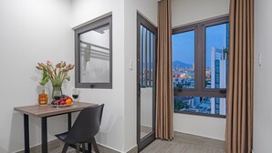 Una habitación moderna con una mesa de comedor, una silla, un florero con flores y vistas a un paisaje urbano a través de ventanas amplias.