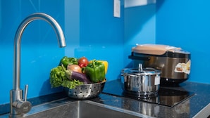 Una cocina con pared azul, un lavamanos de acero inoxidable, un colador con vegetales y una olla sobre la estufa.