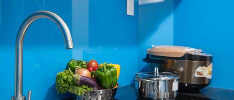 A kitchen with a blue wall, a stainless steel sink, a colander with vegetables, and a pot on the stove.